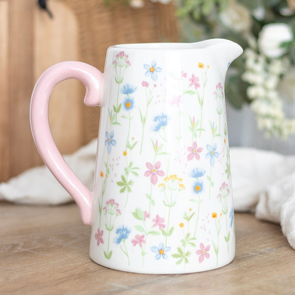 Ceramic pitcher with floral pattern and pink handle on a wooden surface