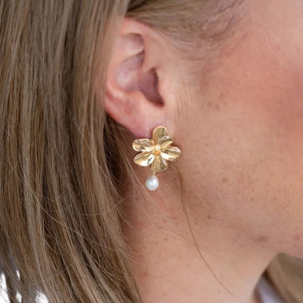 Gold flower-shaped earring with a pearl on an ear
