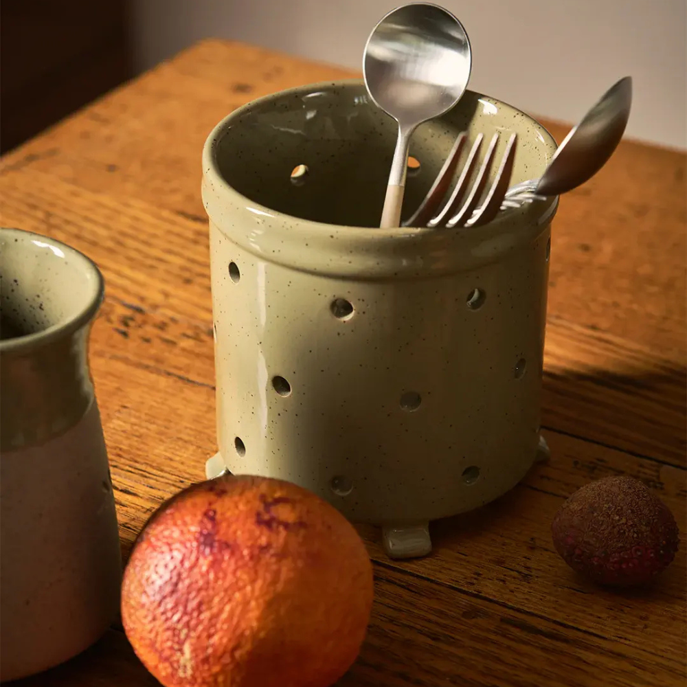 Ceramic utensil holder with cutlery on a wooden surface with fruits.