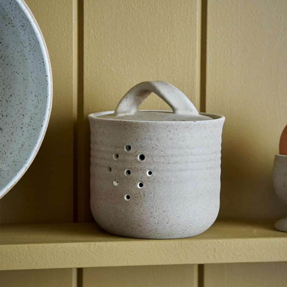 Speckled ceramic canister with handle on a wooden shelf against a beige wall