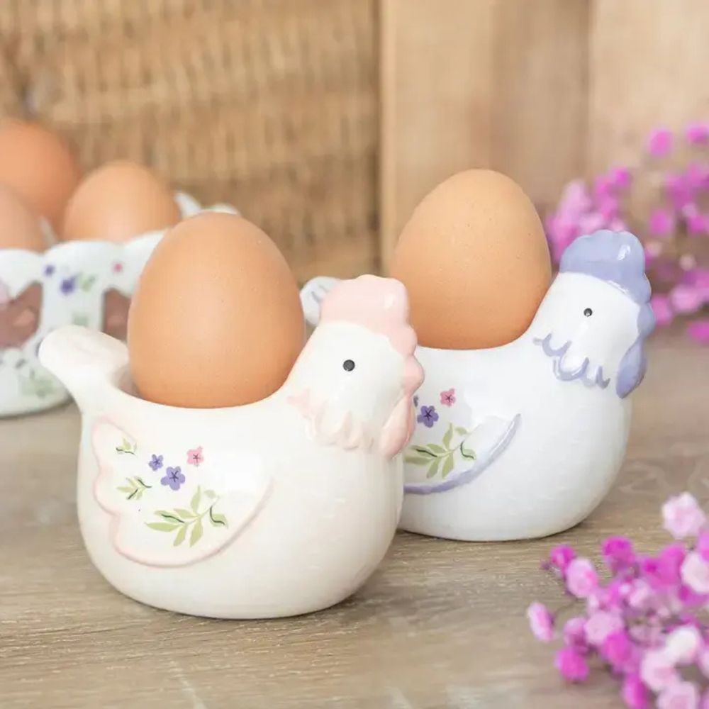 Two ceramic chicken-shaped egg holders with eggs on a wooden surface.