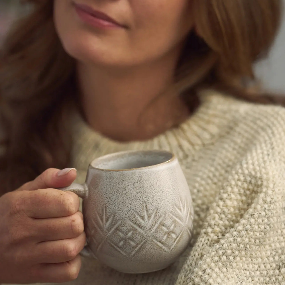 Person holding a textured ceramic mug with a neutral background