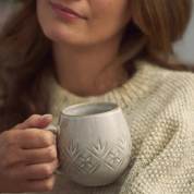 Person holding a textured ceramic mug with a neutral background