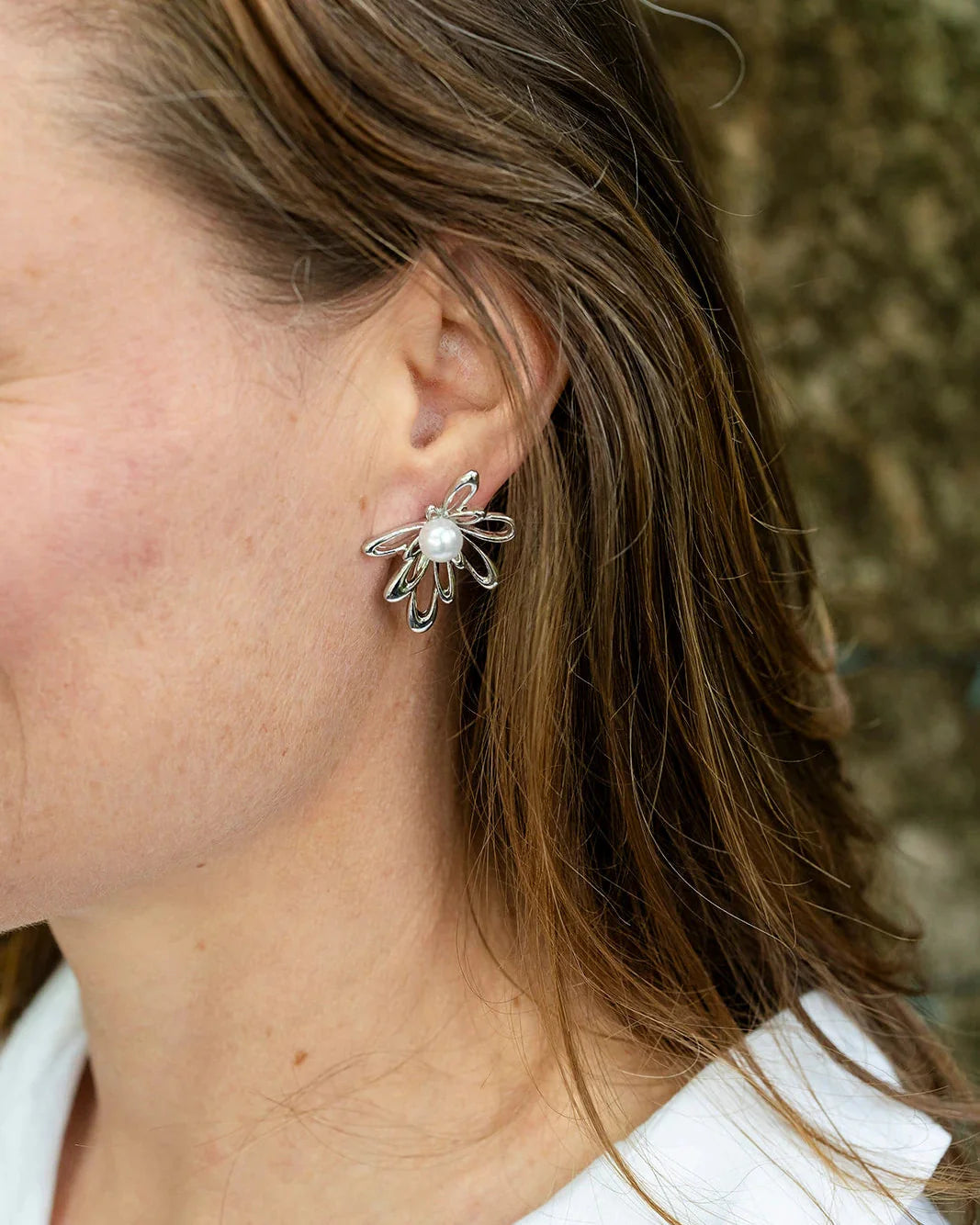 Close-up of a person wearing a silver earring with a pearl-like center.