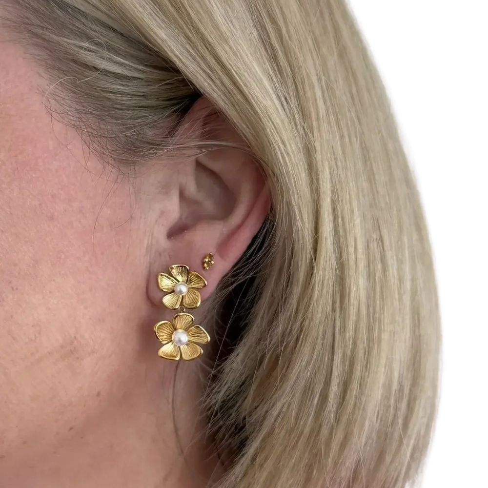 Gold flower-shaped earrings with pearl centers worn by a person with blonde hair.