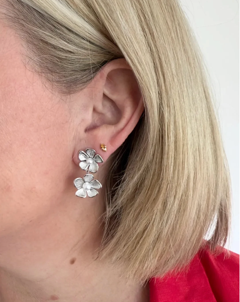 Close-up of a person wearing silver flower-shaped earrings with pearl centres