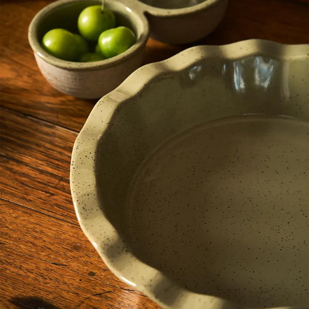 Speckled ceramic pie dish on a wooden surface with a small bowl of green apples.