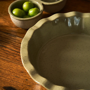 Speckled ceramic pie dish on a wooden surface with a small bowl of green apples.
