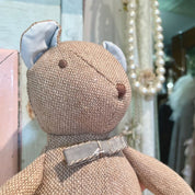Textured teddy bear with a silver bow tie in a blurred indoor setting
