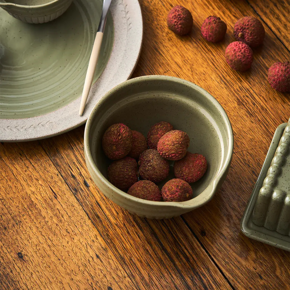 Bowl of lychees on a wooden table with a green ceramic dish and spoon.